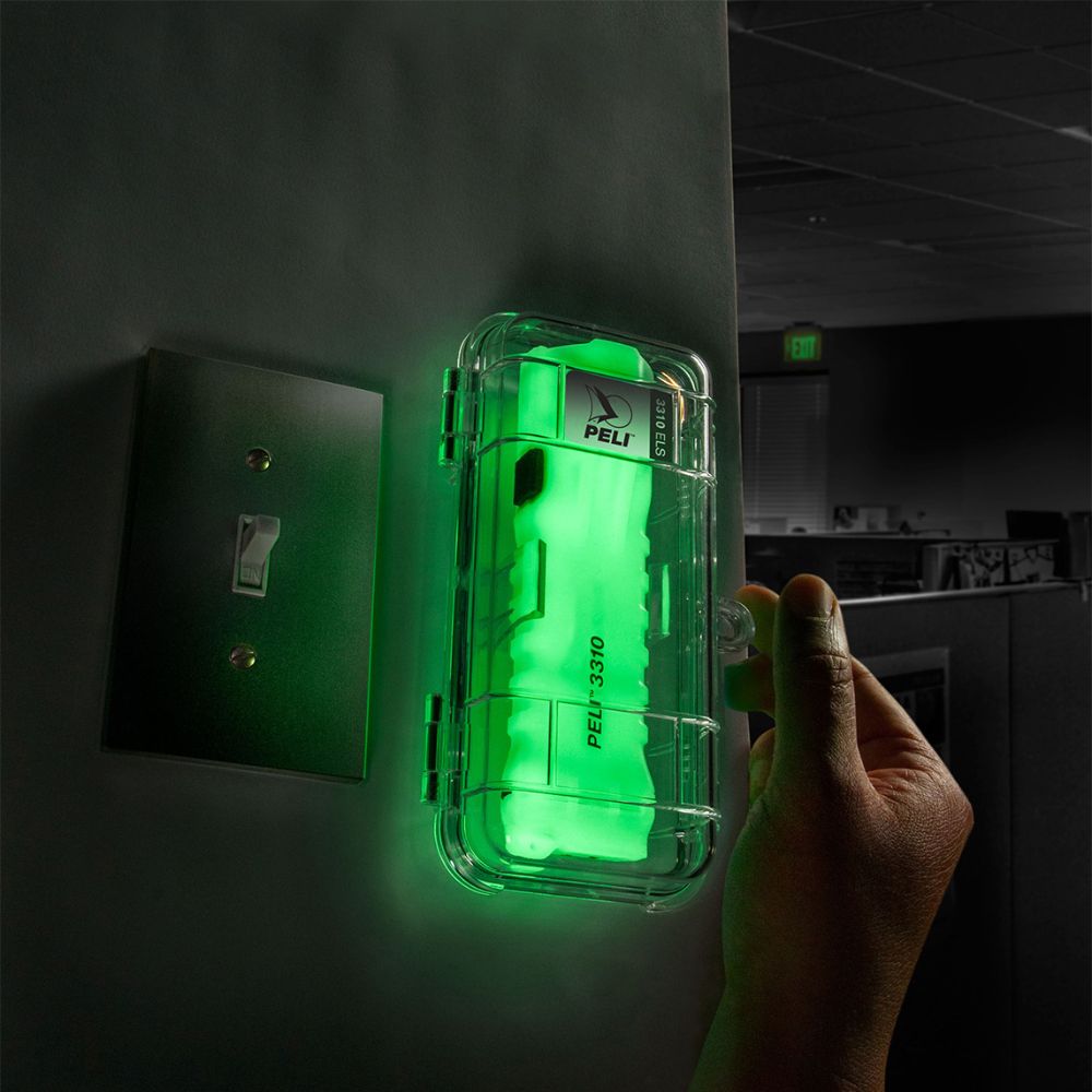 Hand adjusting a bright green Peli emergency light in a clear protective case on an office wall beside a switch.